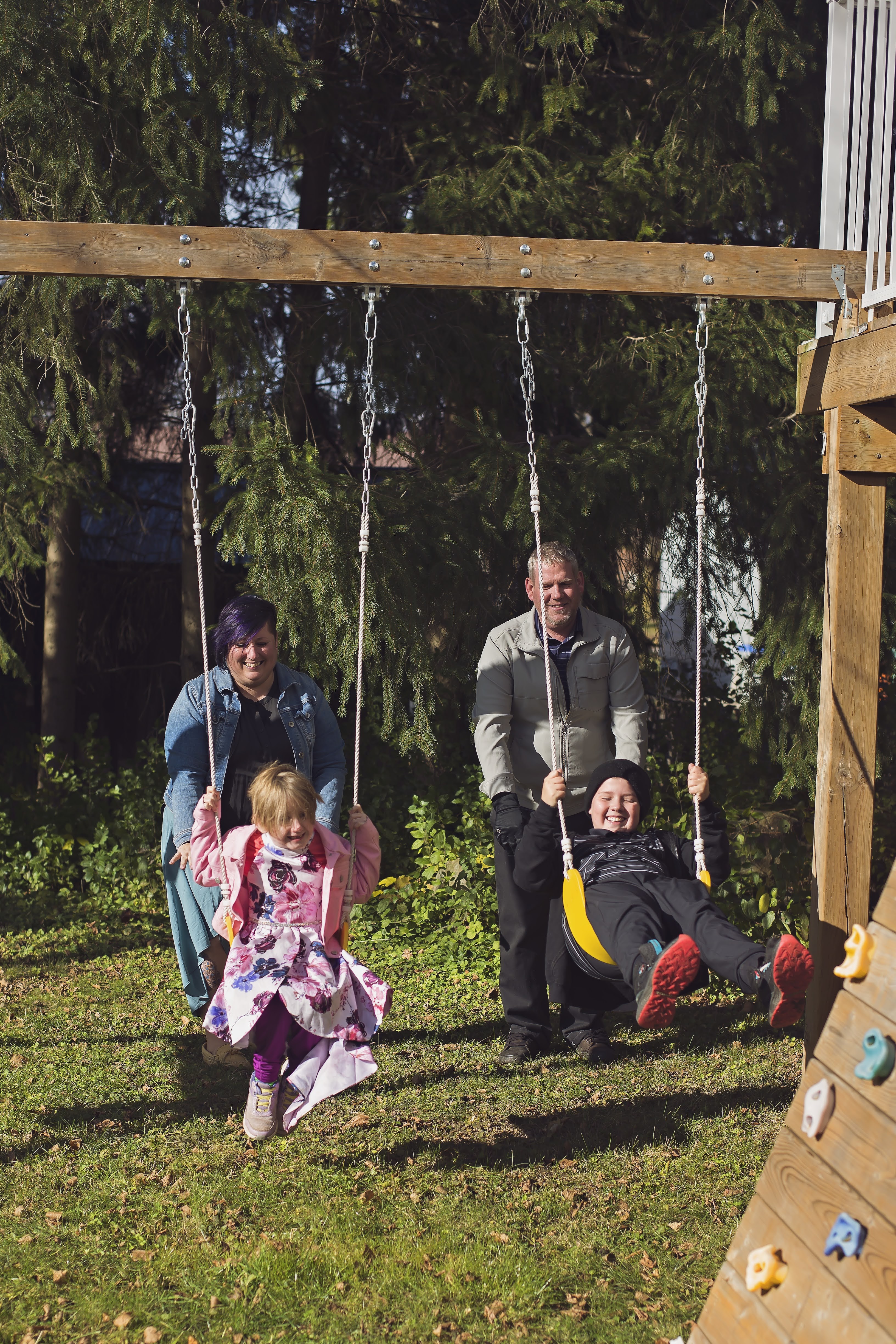 Kathleen and her husband pushing their two daughters on a swingset.